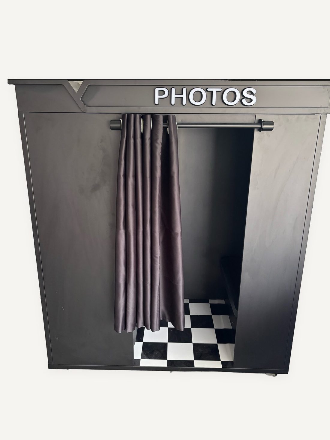 Black sit-in photo booth with a PHOTOS sign, curtain, and checkered floor