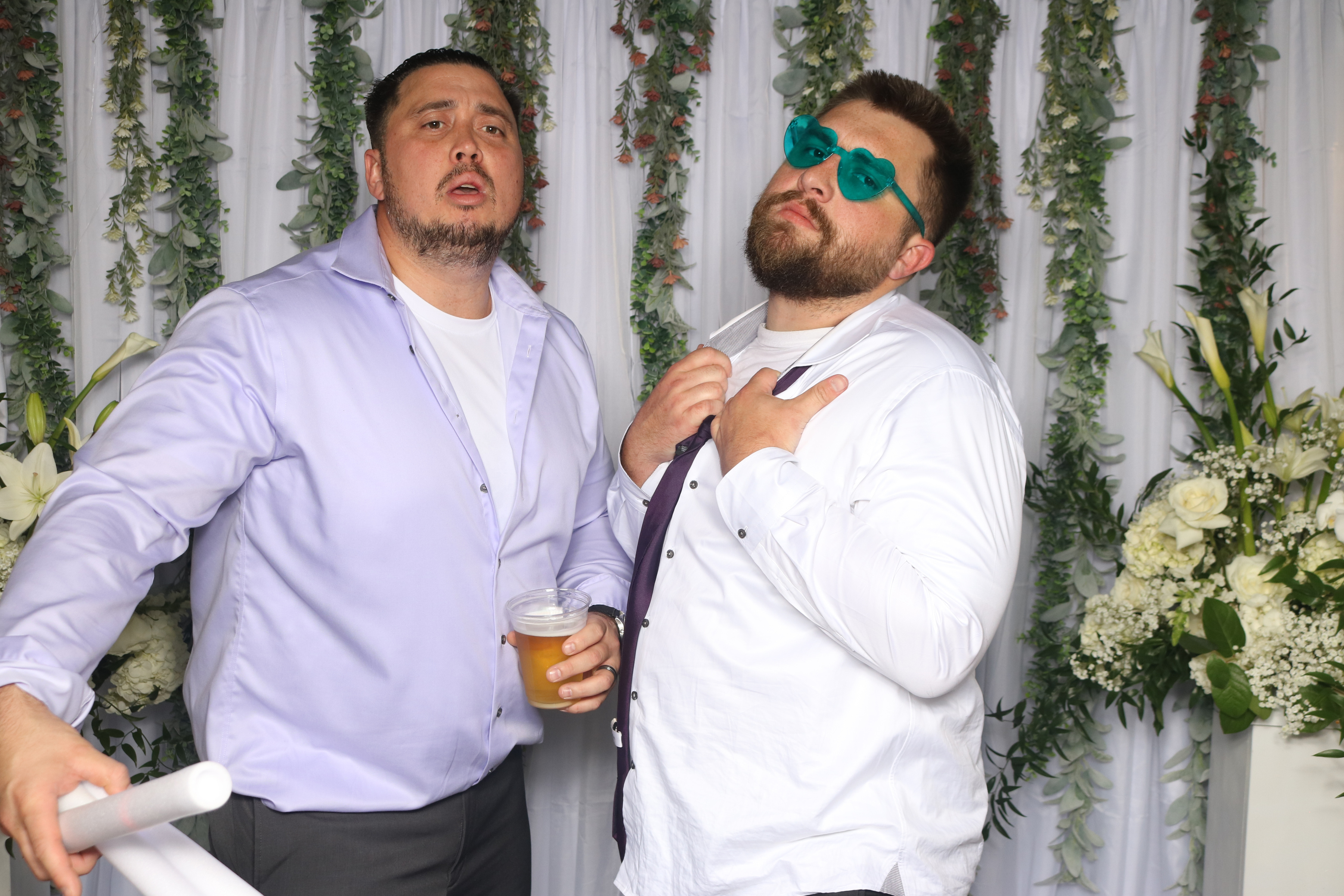 Guests posing in the Picture Perfect Events wedding photo booth with a white backdrop and floral garland
