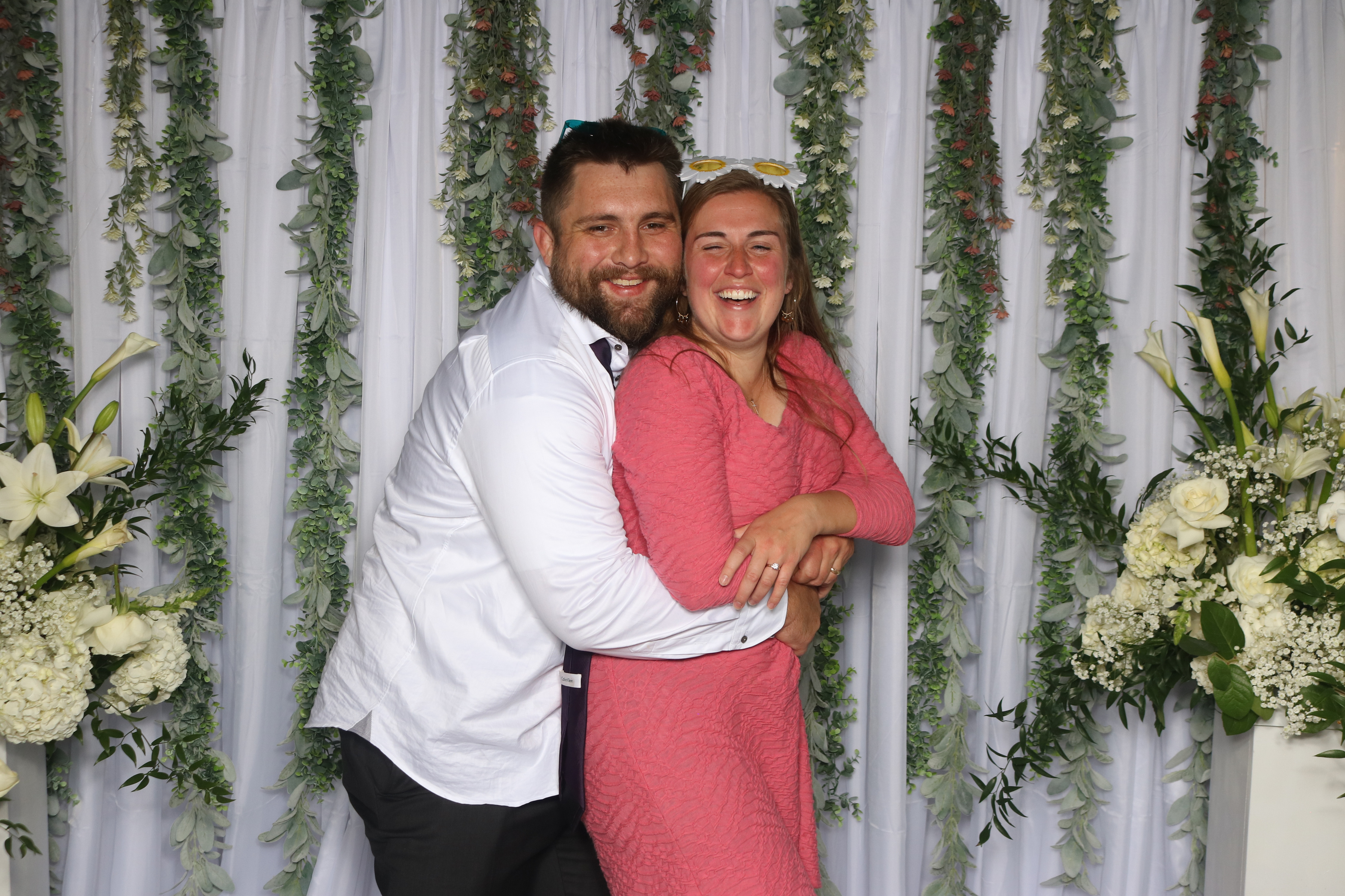 Couple laughing in the wedding photo booth with greenery and flowers